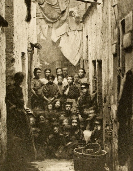 Poor women with young children in a small dingy Glasgow close. Washing and sheets hang from poles above their heads.